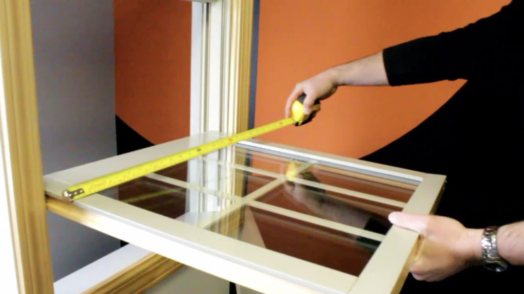 A person measuring a wooden window sash with a yellow tape measure.