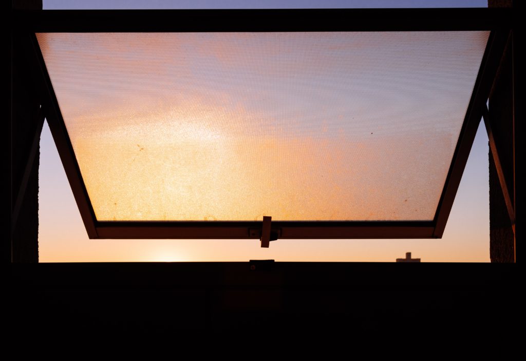 A sunset through the silhouette of an open awning window.